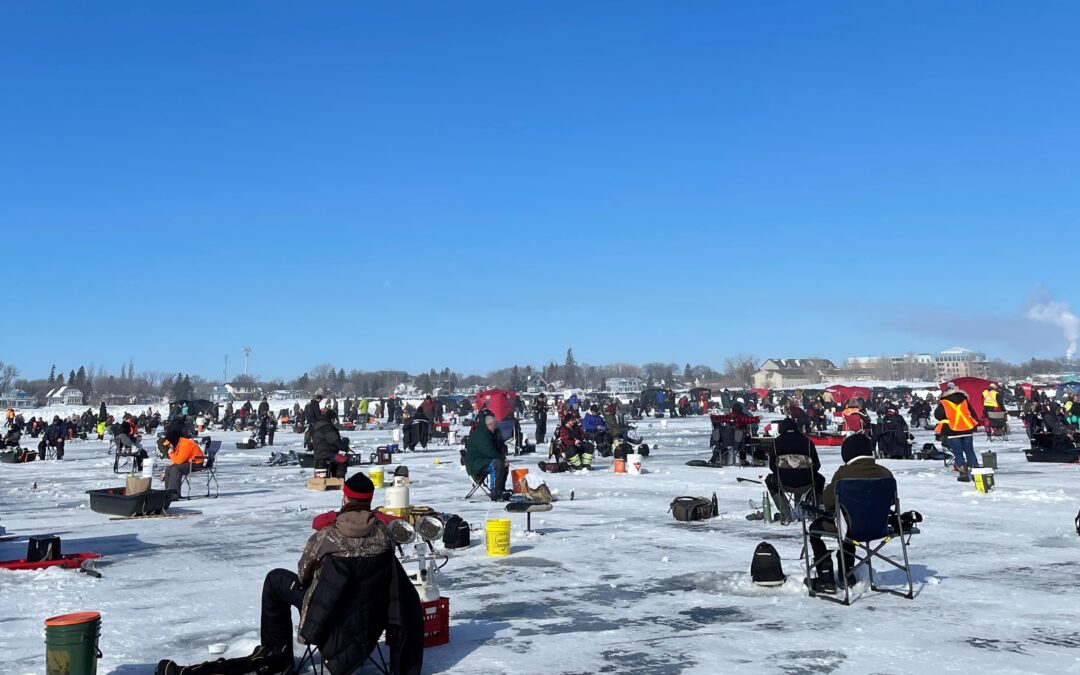 Image is a wide shot of a frozen lake with many people ice fishing.